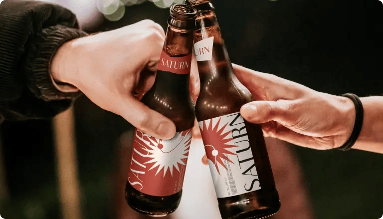 Two people clinking Saturn beer bottles with custom label designs