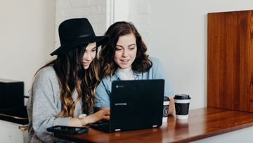 Women sitting by the samsung laptop and working together - two cups of coffee by the side