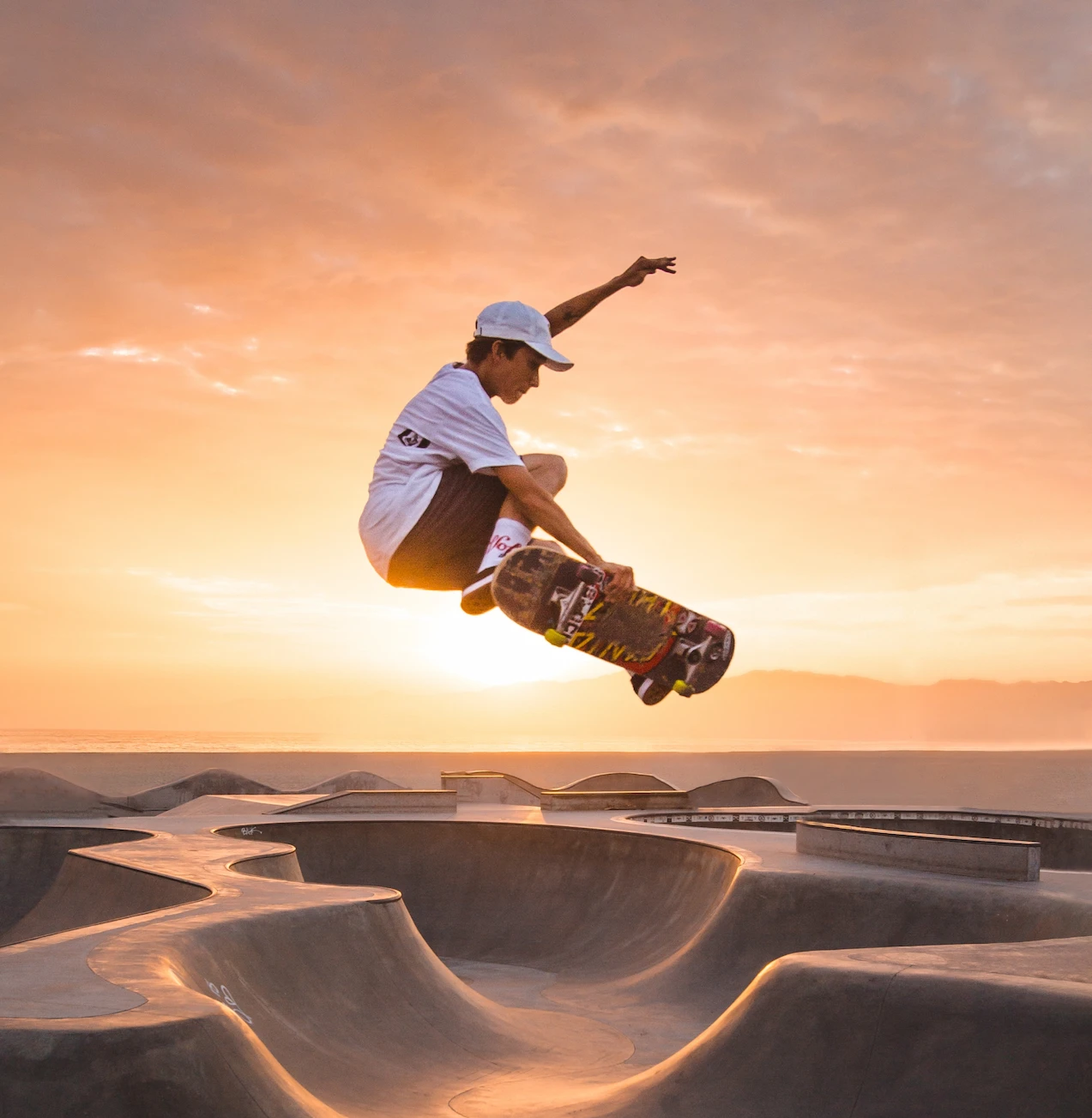 man on a skateboard skating above skatepark by the sunset